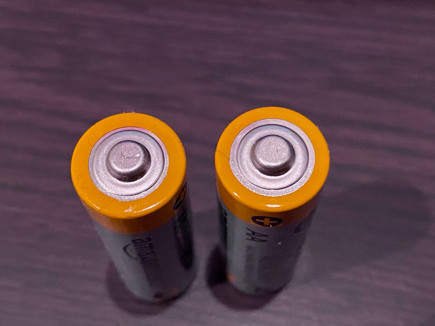 Two AA batteries viewed from above on a dark wooden surface