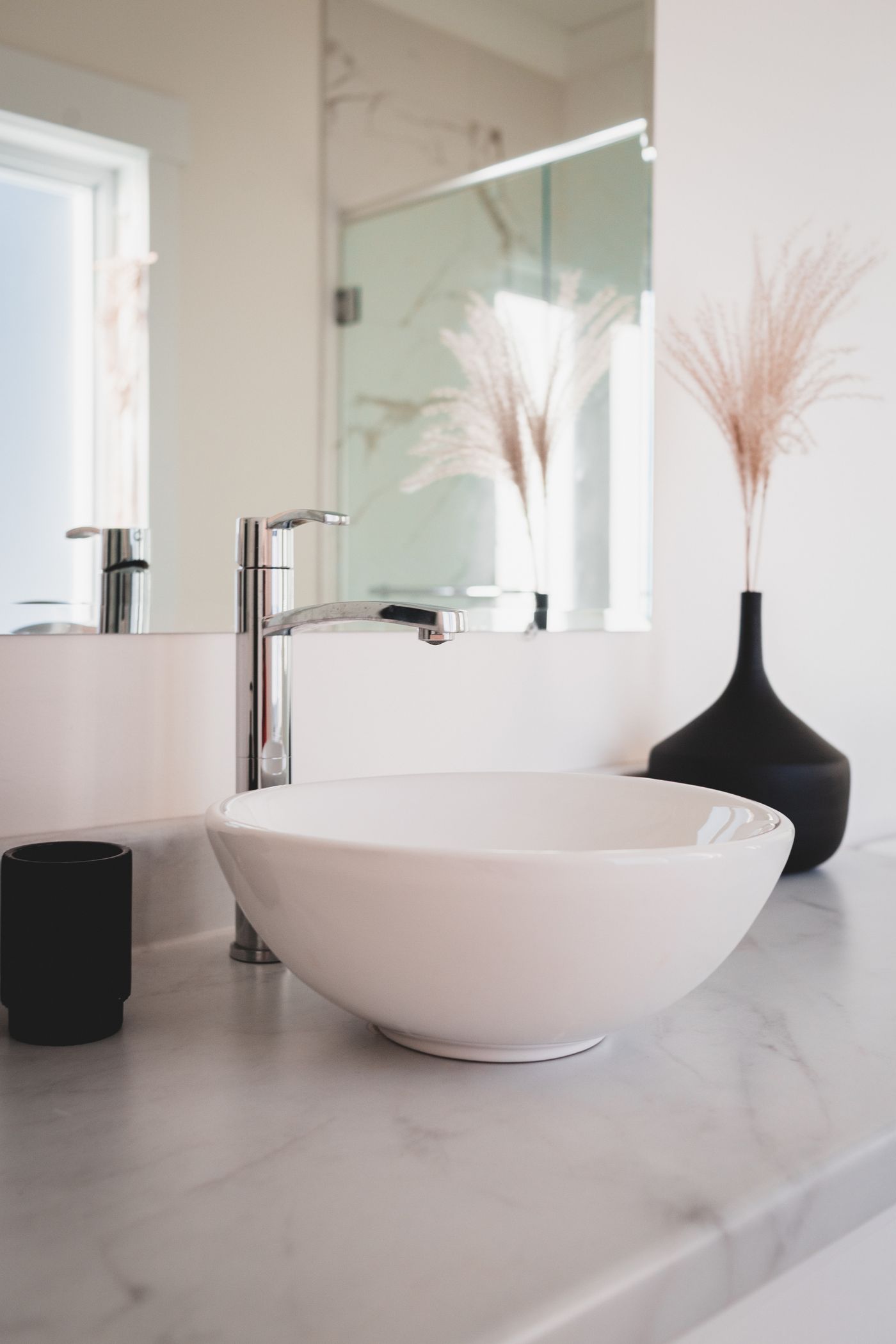 A washbasin with a dark decorative vase and dried stems