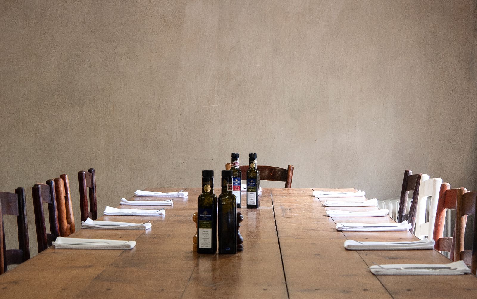 A long table set with napkins, utensils, and oil bottles