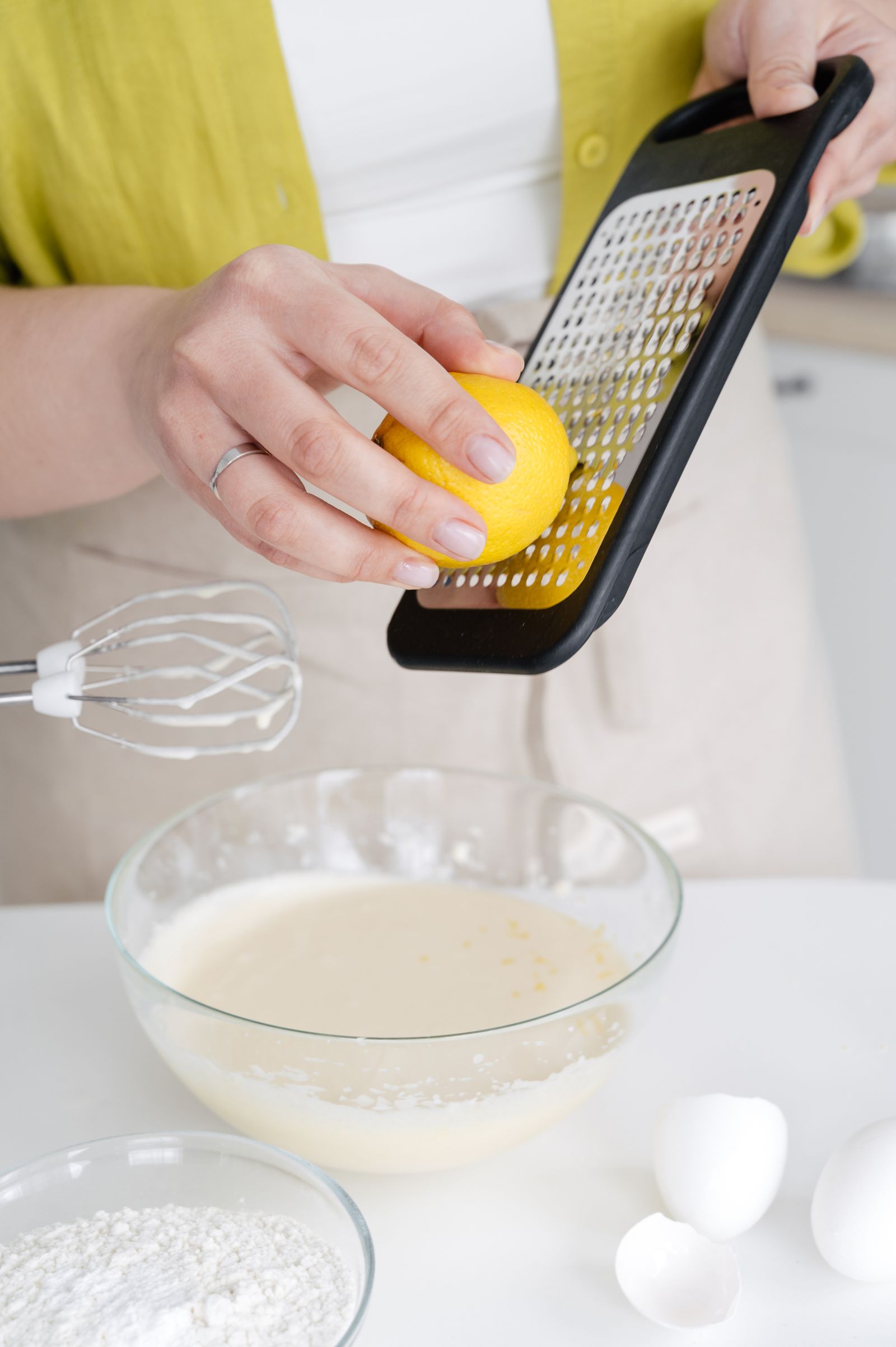 A person grating lemon peel into a mixing bowl