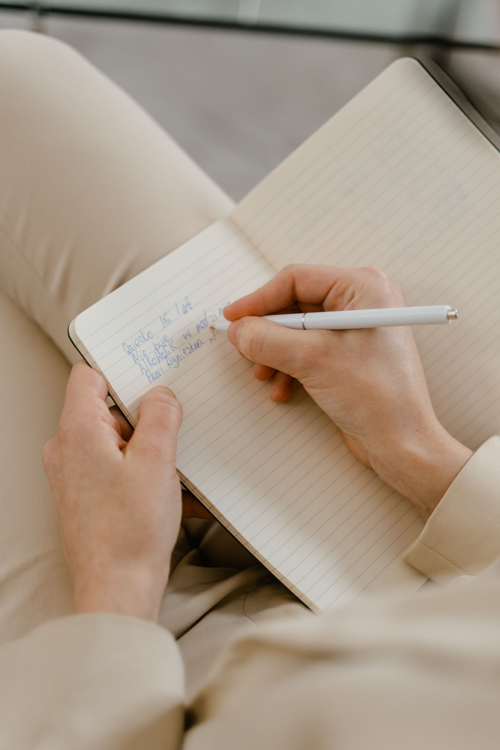 A hand writing in a lined notebook with a pale pen
