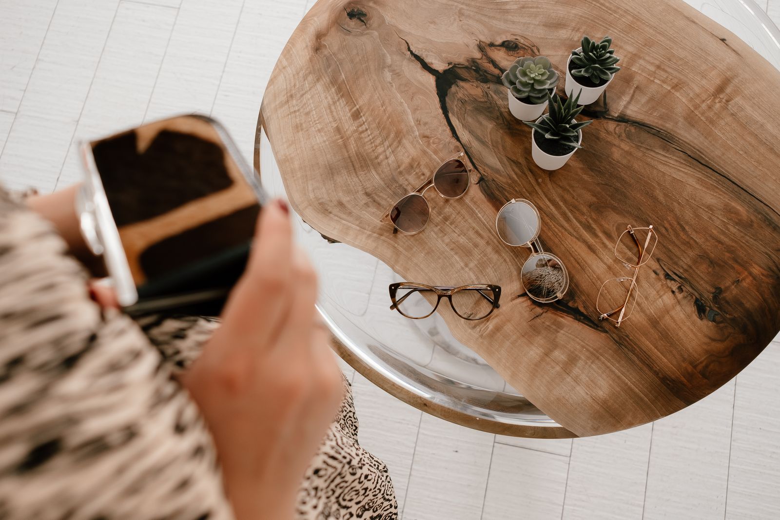 Glasses resting on a round wooden table beside a person holding a phone