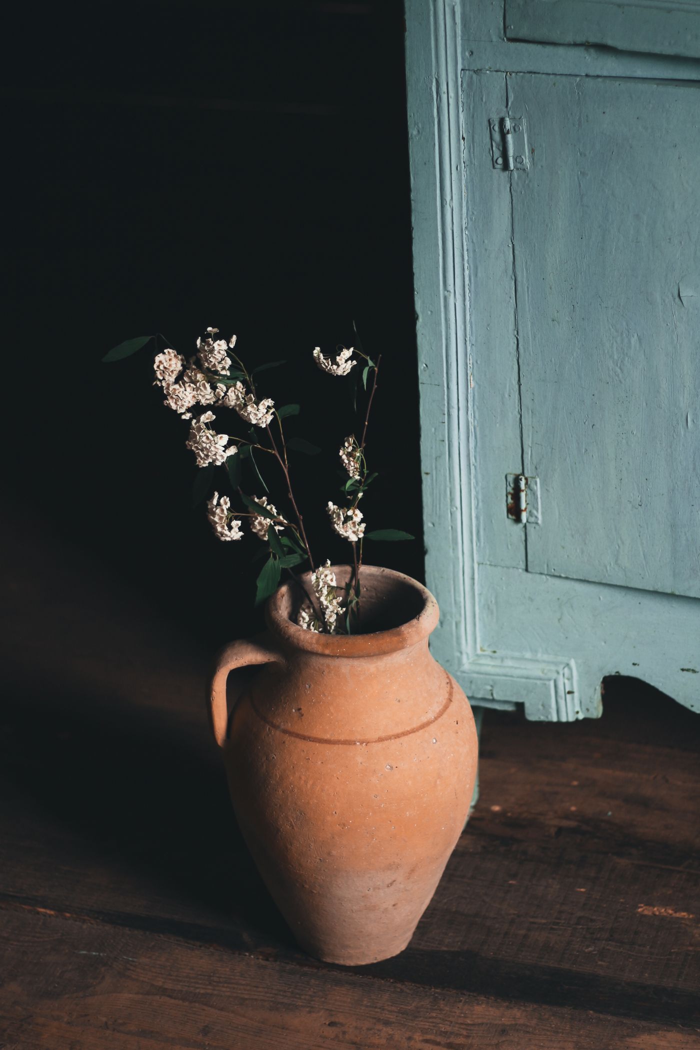 Clay vessel with branches standing beside a cabinet