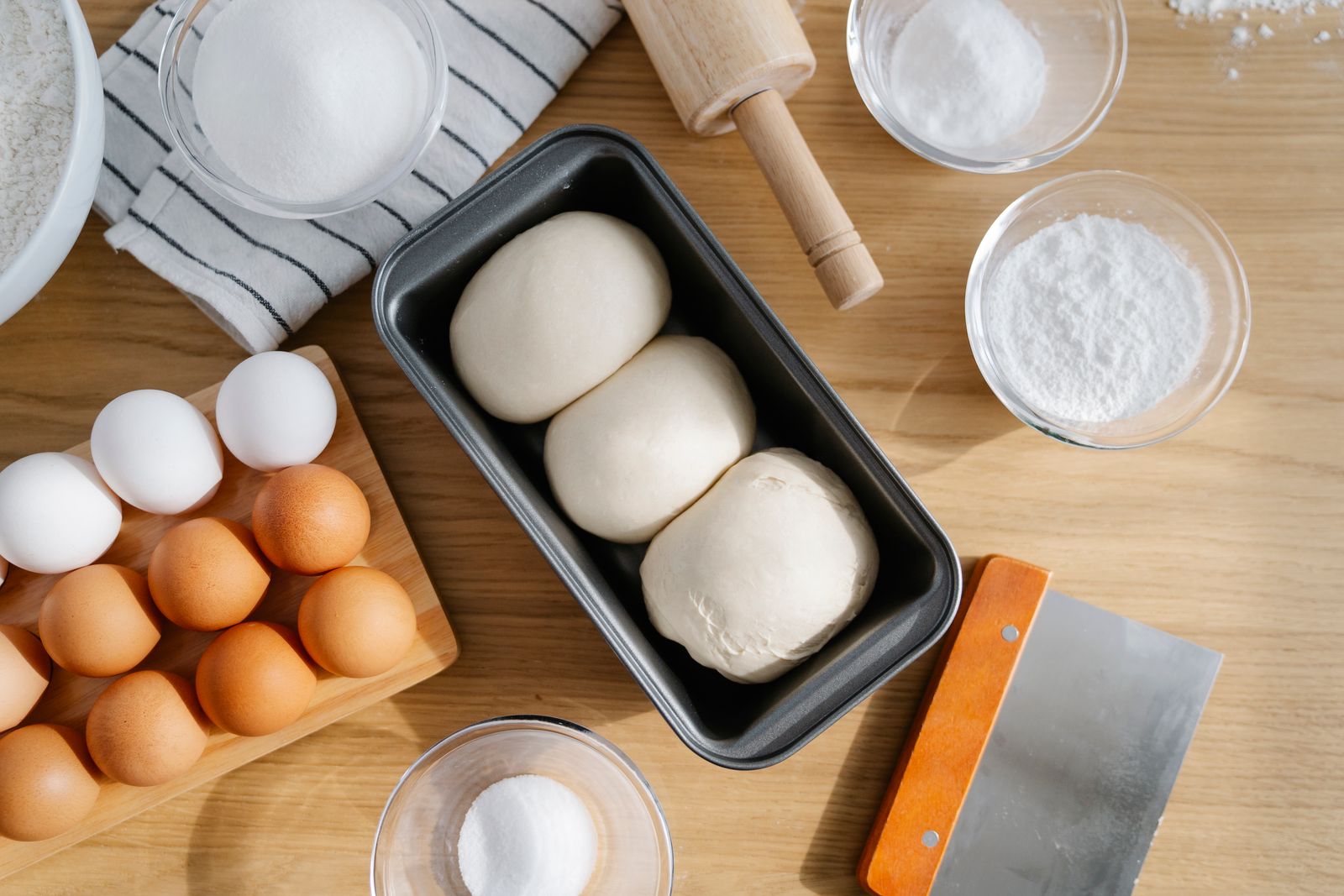 Two dough portions in a loaf pan beside eggs and flour