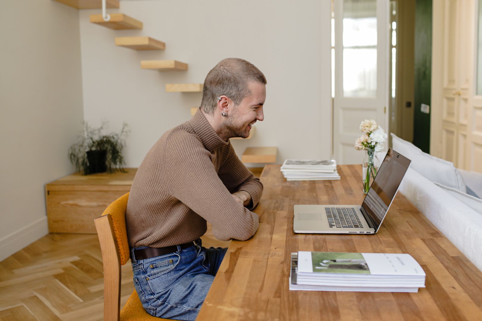 A person using a laptop at a wooden table near stairs