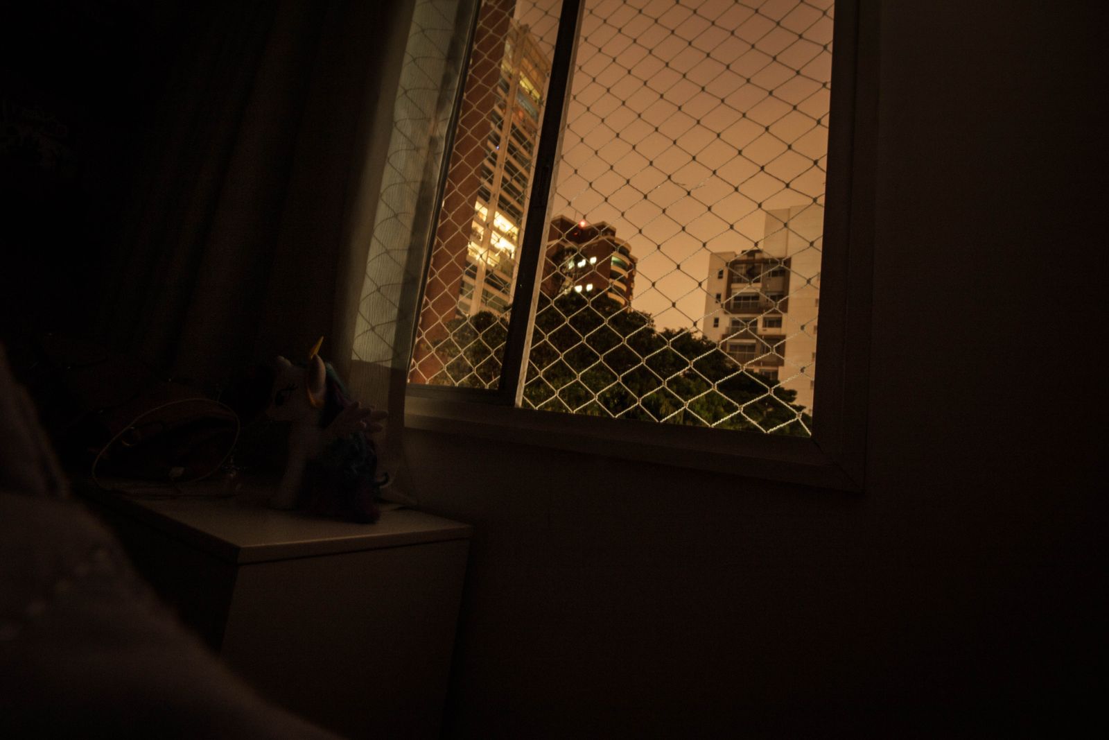 A dark room with a window covered by diamond-pattern wire mesh
