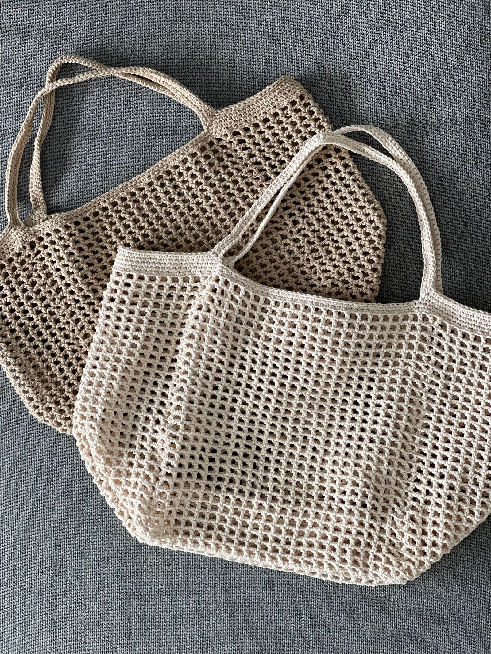 Two reusable knitted mesh bags on a gray surface