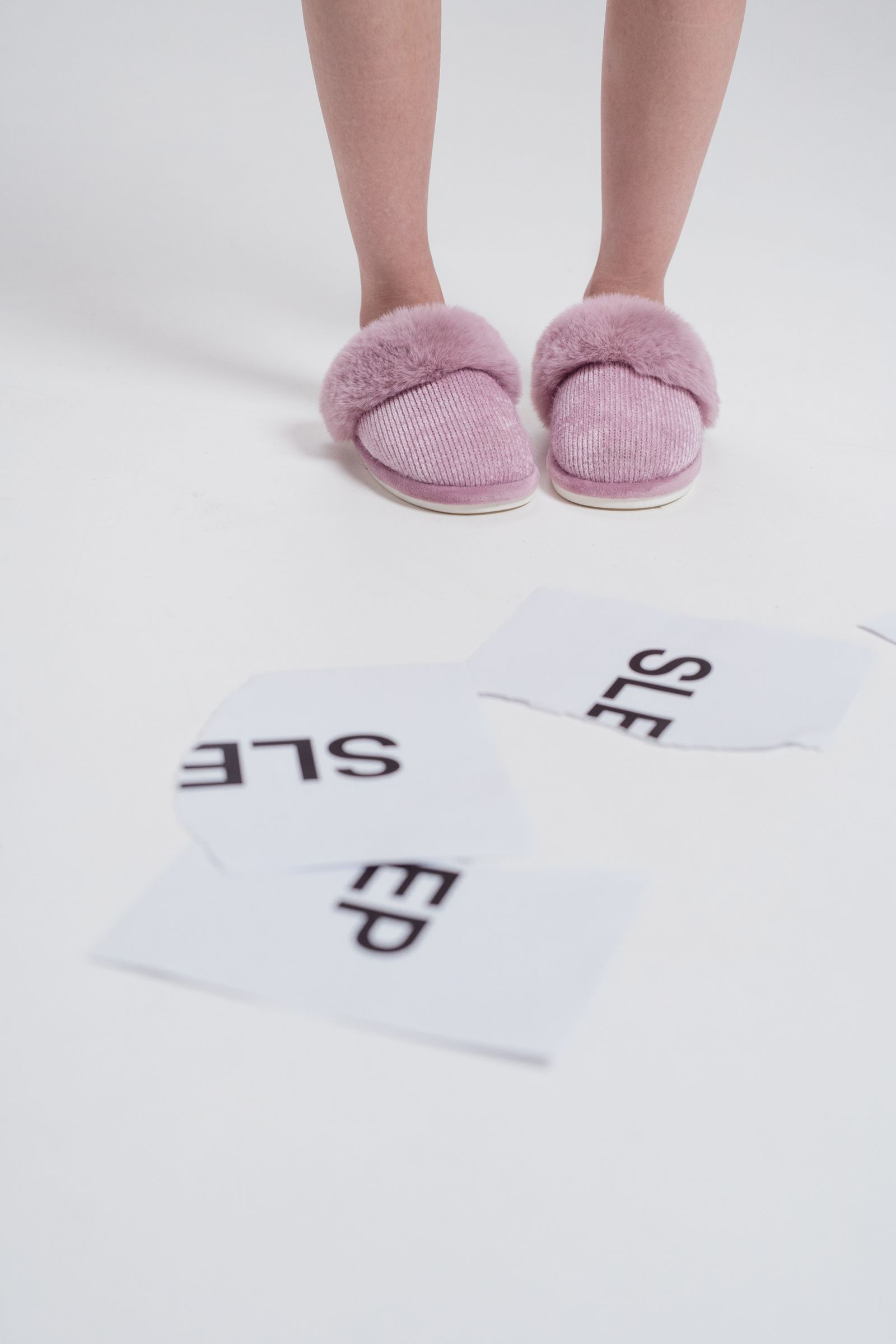 A person wearing pink slippers above white paper sheets