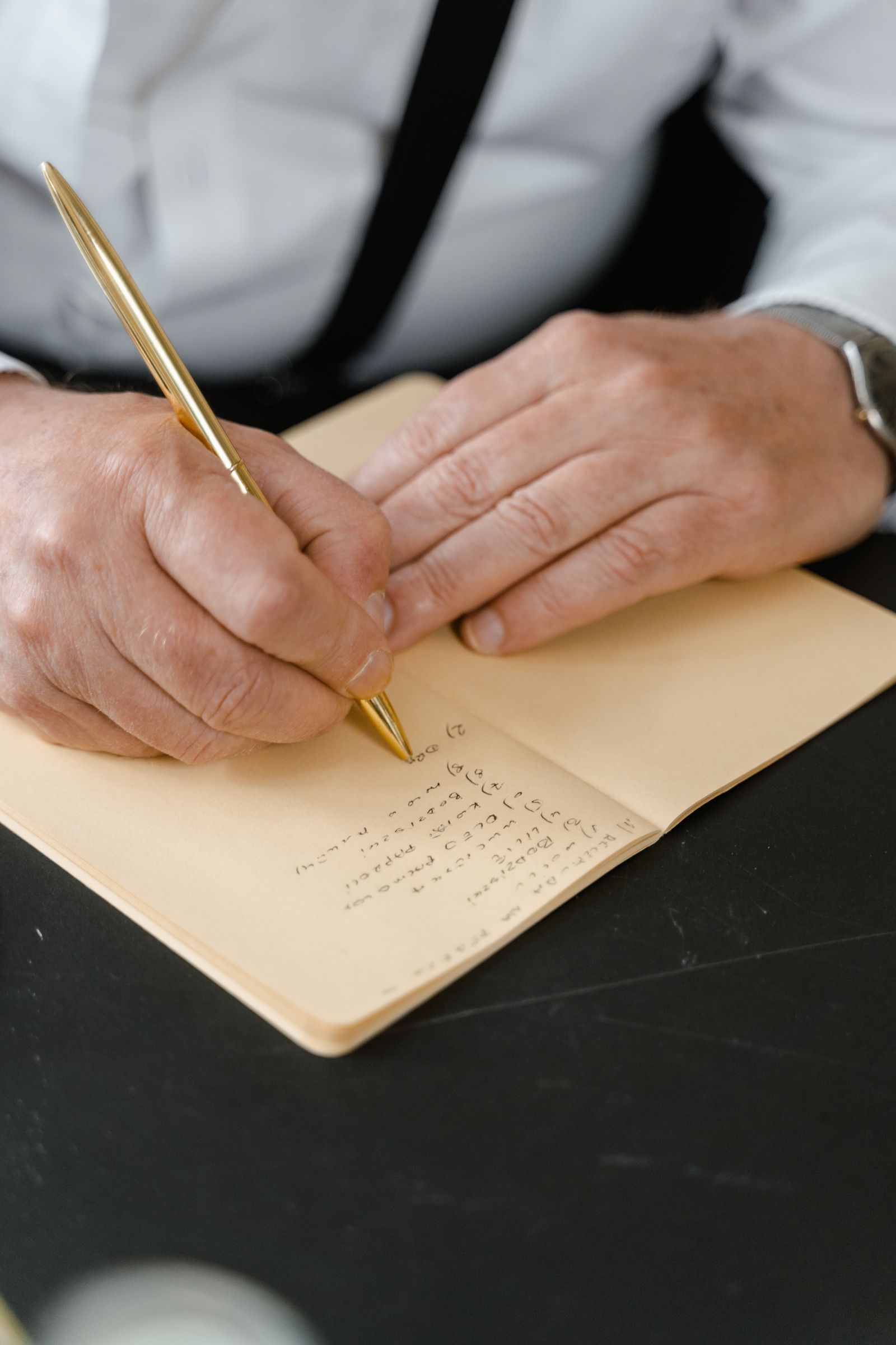 Hands writing in an open notebook with a gold-colored pen