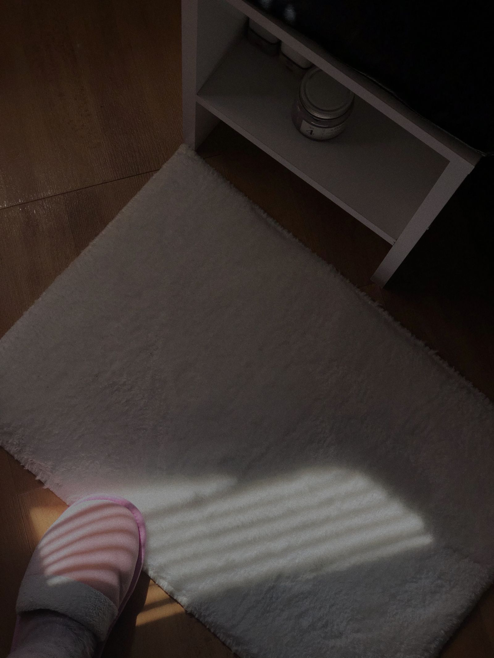 Striped slippers at the edge of a bedroom rug in window light