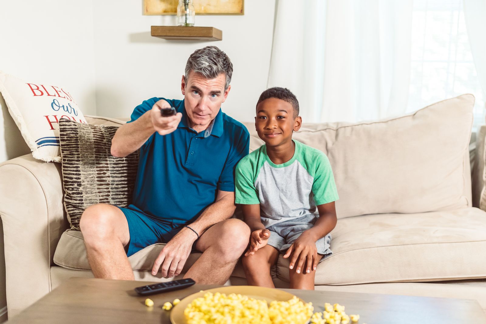 An adult holding a remote beside a child on a sofa