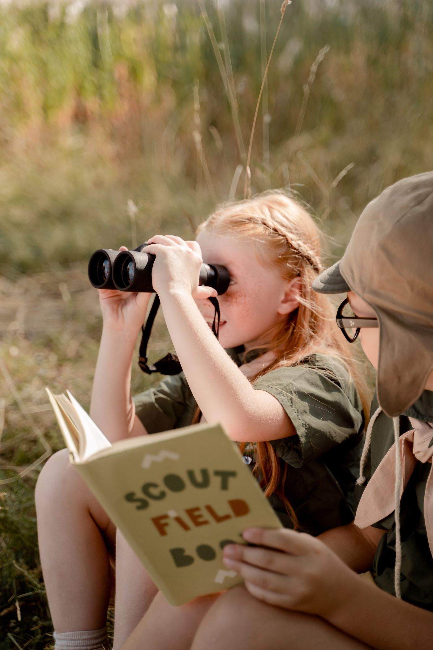 Young observer holding binoculars and a field notebook outdoors