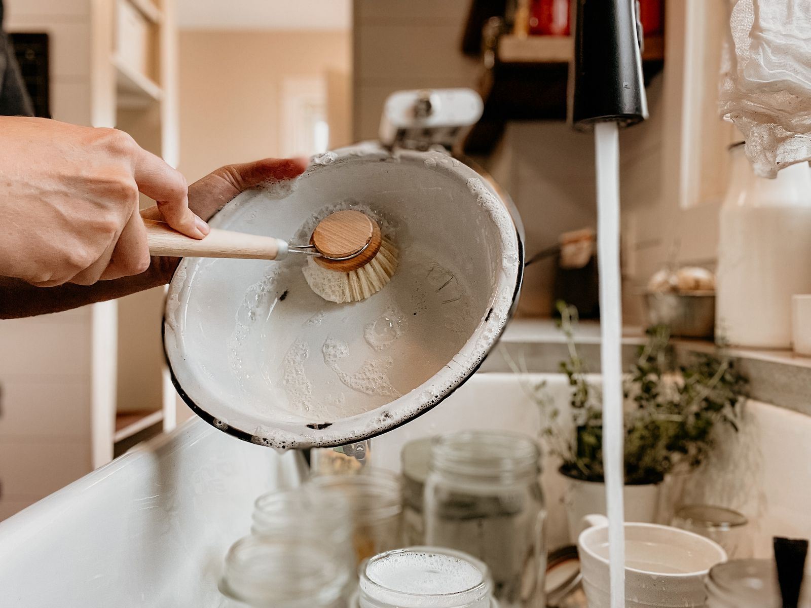 Hands washing a bowl with a brush at a kitchen sink